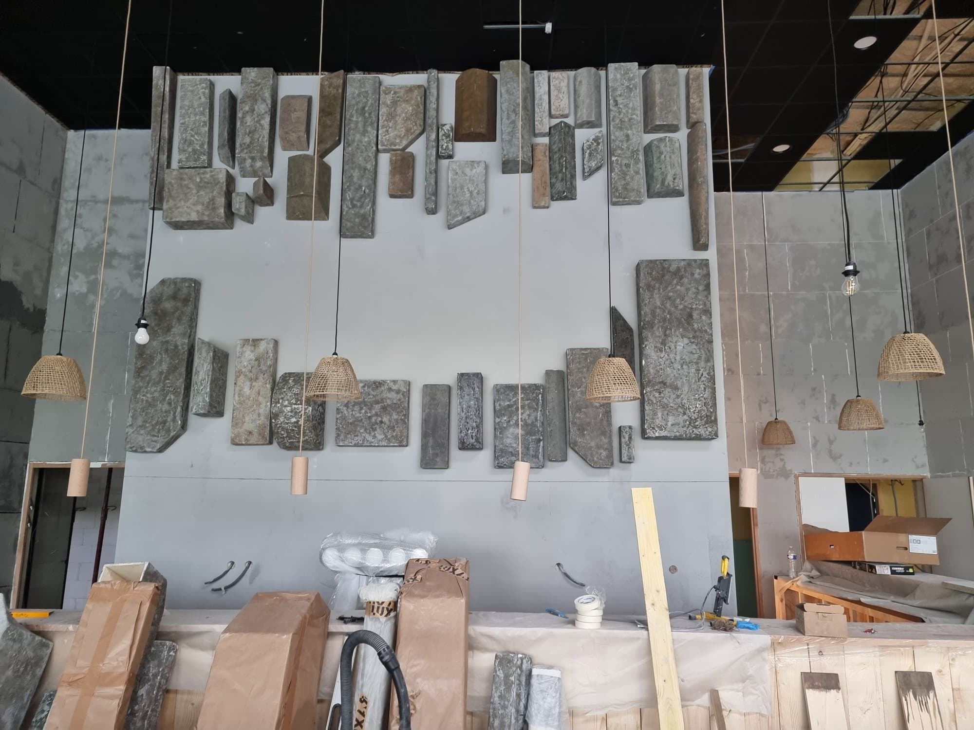 The wall of hanging panels and its pendant lights, being installed